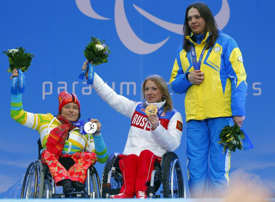 Ukraine's Olena Iurkovska covers her bronze medal with her hand after finishing third in the women's biathlon 12,5 km sitting event as she and first place Svetlana Konovalova of Russia, center and second place Anja Wicker of Germany pose during a medal ceremony at the 2014 Winter Paralympics, Friday, March 14, 2014, in Krasnaya Polyana, Russia. The majority of Ukraine's Paralympic medalists covered their medals during medal ceremonies. (AP Photo/Dmitry Lovetsky)