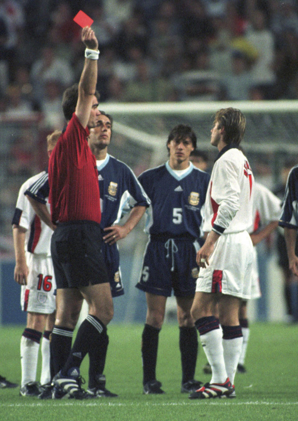 ARCHIVO - El jugador inglés David Beckham recibe una tarjeta roja del árbitro danés Kim Milton Nielsen por patear al jugador argentino Diego Simeone, durante el partido de fútbol de segunda ronda de la Copa Mundial entre Inglaterra contra Argentina, en Saint Etienne, Francia, el 30 de junio de 1998. Inglaterra perdió en penales después de que terminó el partido 2 -2. La serie documental de Netflix, "Beckham", que se estrena el 4 de octubre de 2023, explora la crianza de Beckham, sus triunfos y tropiezos. (Foto AP/Denis Doyle, archivo)