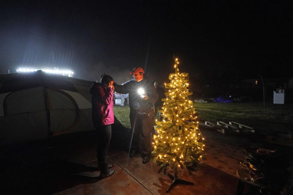 Tiffany Theriot, right, founder of the charity Cajun Commissary, surprises Cristin Trahan with a Christmas tree donated by a volunteer, on the property of their destroyed home in Lake Charles, La., Friday, Dec. 4, 2020. Cristin, her husband and a son are living in tents on the property, while her other son, his fiancée and their one-year old son are living in a loaned camper there. A relative's home on the same property is now gutted and they are living in a camper as well. (AP Photo/Gerald Herbert)