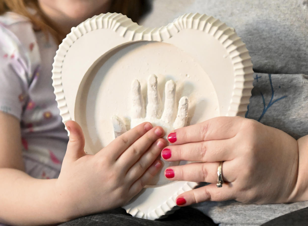 Jessica Day-Weaver right, and Caitlin Weaver hold up a ceramic hand print of daughter, Anastasia, at their home, Thursday, Feb. 2, 2022, in Boardman, Ohio.(AP Photo/Nick Cammett)