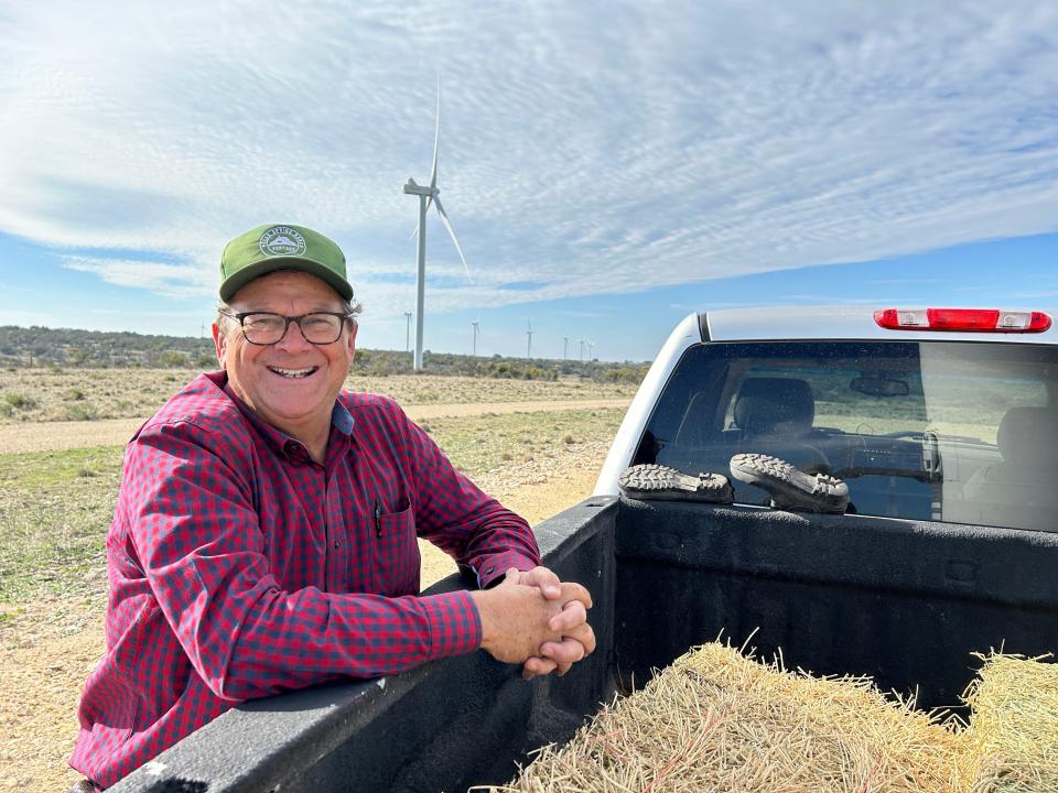 John Davis leans on his truck. Behind him are wind turbines at his ranch in Concho County, Texas.