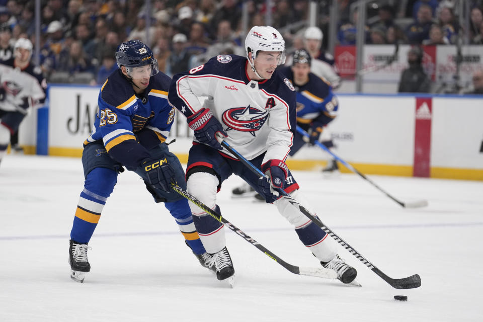 Columbus Blue Jackets' Zach Werenski (8) and St. Louis Blues' Jordan Kyrou (25) battle for a loose puck during the second period of an NHL hockey game Tuesday, Jan. 30, 2024, in St. Louis. (AP Photo/Jeff Roberson)