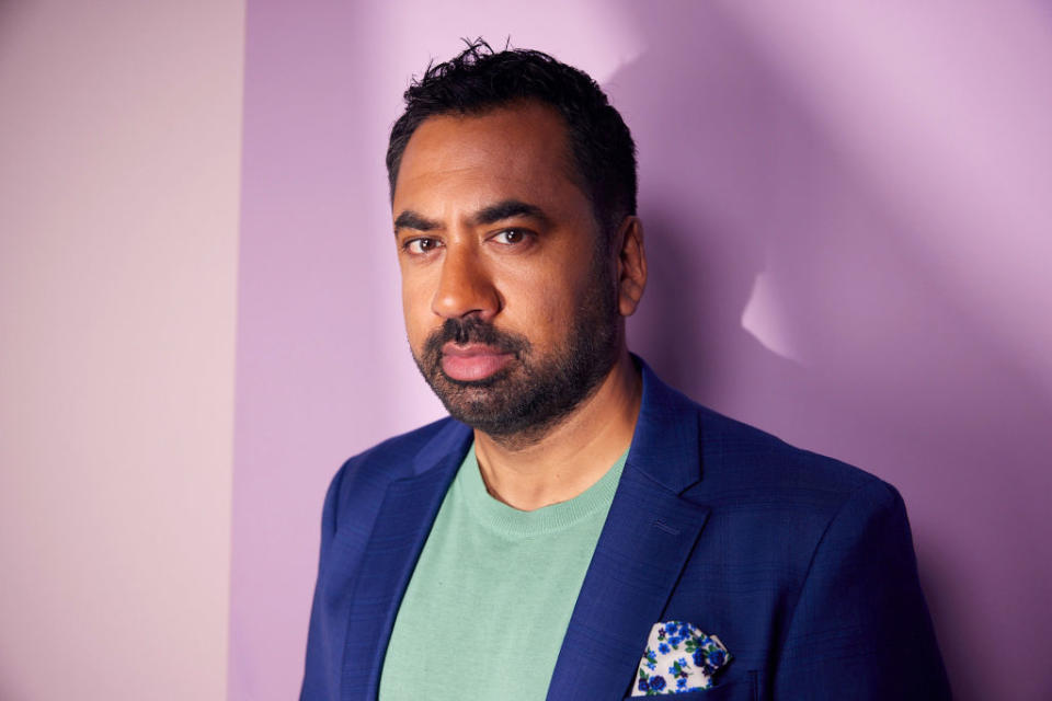 Kal Penn in a casual green T-shirt under a navy blazer, standing against a plain background