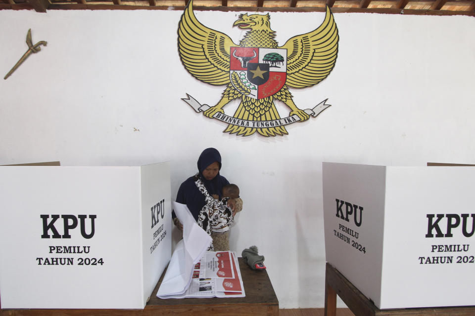 A woman checks her ballots as Indonesia's national emblem 'Garuda Pancasila' is seen hanging on the wall at a polling station during the election in Yogyakarta, Indonesia, Wednesday, Feb. 14, 2024. Indonesian voters were choosing a new president Wednesday as the world's third-largest democracy aspires to become a global economic powerhouse a quarter-century after shaking off a brutal dictatorship. (AP Photo/Slamet Riyadi)