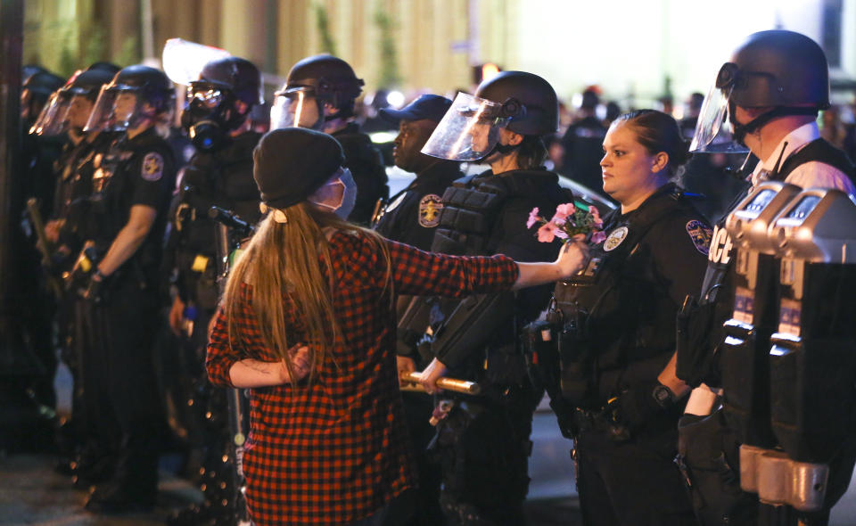 In this Thursday, May 28, 2020, photo, a protester offers a Louisville Metro Police Department officer flowers during a protest at Jefferson Square in Louisville, Ky. (Michael Clevenger/Courier Journal via AP