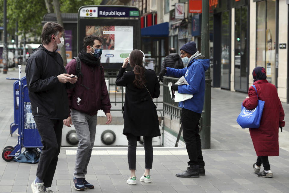 A newspaper street vendor wearing a face mask talks to a passerby, Monday, May 11, 2020 in Paris. The French began leaving their homes and apartments Monday for the first time in two months without permission slips as the country began cautiously lifting its virus lockdown. (AP Photo/Thibault Camus)