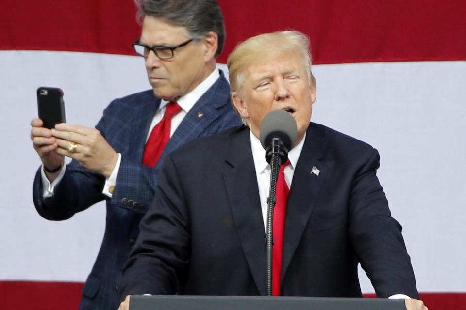 FILE - In this July 24, 2017, file photo, President Donald Trump delivers a speech to scouts as Secretary of Energy Rick Perry uses his phone at the 2017 National Boy Scout Jamboree at the Summit in Glen Jean, W.Va. Long after more flamboyant Cabinet colleagues fell out of Trump’s favor amid ethics scandals, low-profile Perry, the folksy former Texas governor, survived in part by steering clear of controversy as energy secretary. (AP Photo/Steve Helber, File)