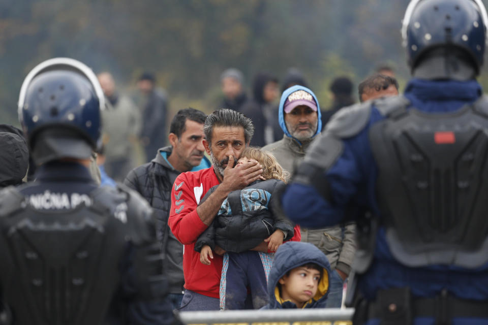 Migrant man holds a child standing in front Bosnian police cordon at the border crossing in Maljevac, Bosnia, Friday, Oct. 26, 2018. About 150 people have gathered at the Bosnian border with Croatia, hoping for the European border to open for people fleeing war and poverty.(AP Photo/Amel Emric)