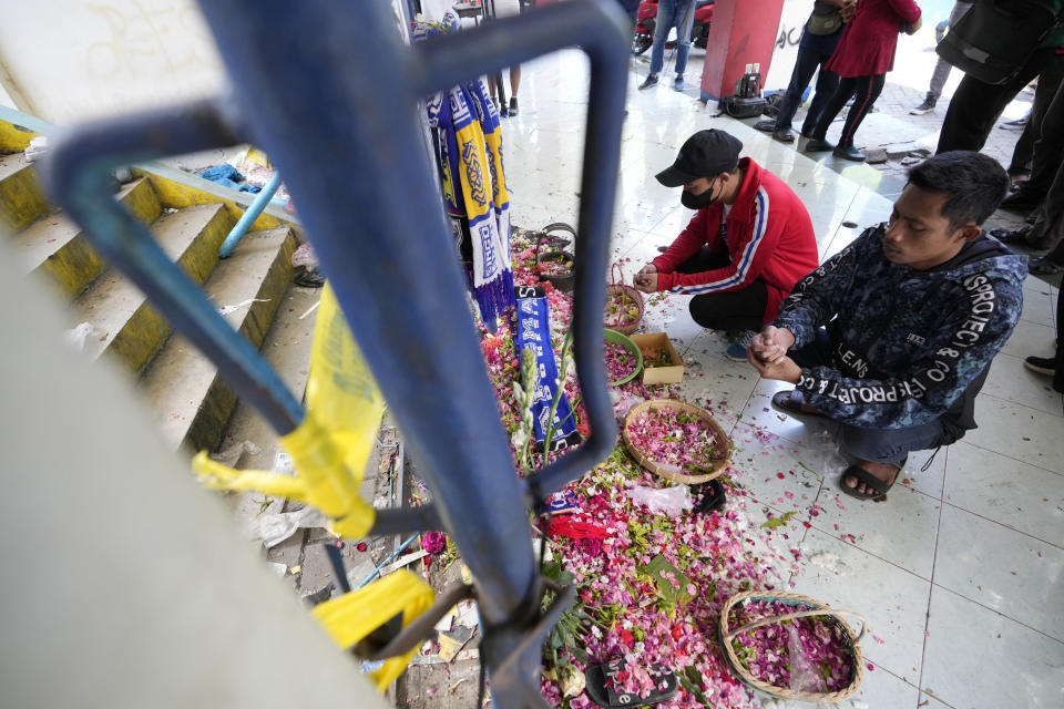 People prays for the victims of Saturday's soccer match stampede in front of gate 13 the Kanjuruhan Stadium in Malang, Indonesia, Tuesday, Oct. 4, 2022. A police chief and nine elite officers were removed from their posts Monday and 18 others were being investigated for responsibility in the firing of tear gas inside a soccer stadium that set off a stampede, killing over 100 people, officials said. (AP Photo/Achmad Ibrahim)