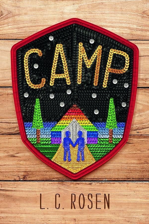 Wooden background featuring a sequined patch. On the patch there is a rainbow house and two blue figures holding hands. Title reads: "Camp."