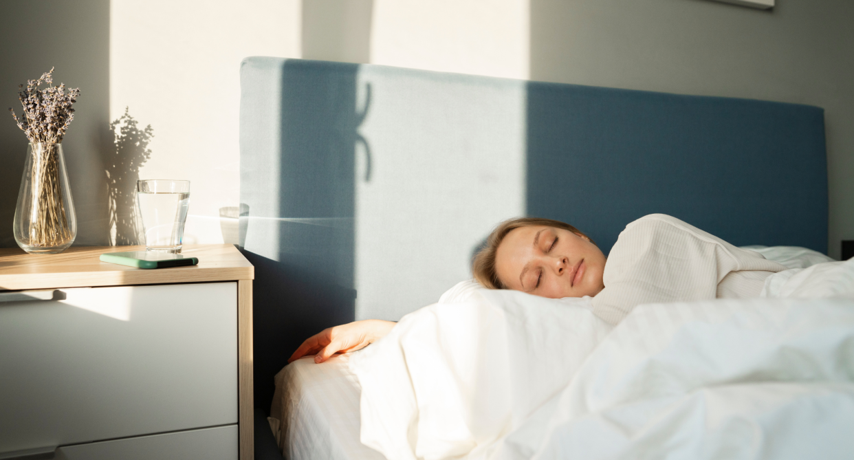 woman sleeping in bed on pillow with white sheets and bedside table 