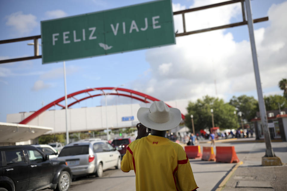 A migrant from Cameroon takes a picture of the Puerta Mexico bridge that crosses the Rio Grande river under a sign that reads in Spanish "Happy travels" in Matamoros, Mexico, Thursday, Aug. 1, 2019, on the border with Brownsville, Texas. The U.S. is sending back groups of 50 to 100 migrants almost daily to Matamoros, according to the state immigration office. (AP Photo/Emilio Espejel)