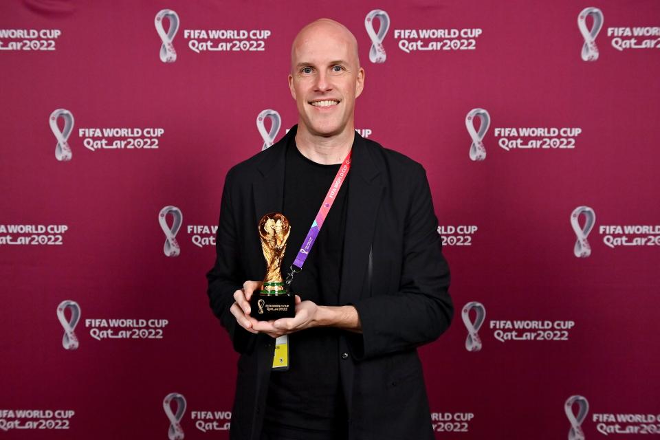 Grant Wahl smiles as he holds a World Cup replica trophy during an award ceremony in Doha, Qatar.