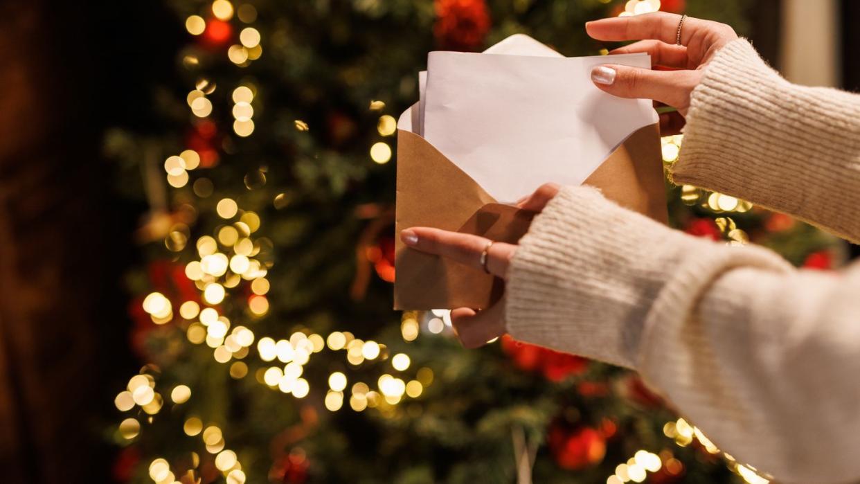 young woman standing by the glistening christmas tree and opening a letter