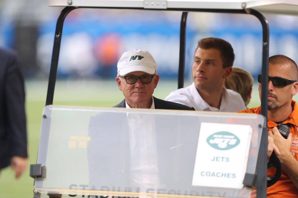 Woody Johnson rides in a golf cart during a preseason game.