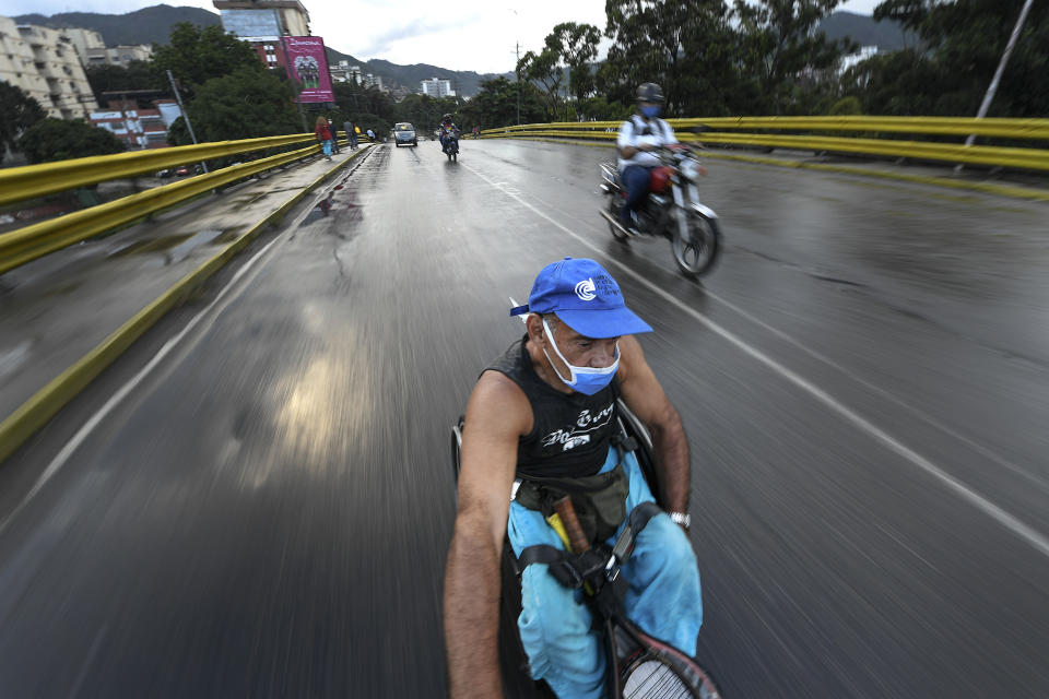 Manuel Mendoza se monta en su silla de ruedas agarrándose a la parte trasera de una motocicleta en el barrio La Paz de Caracas, Venezuela, el lunes 9 de noviembre de 2020. (AP Foto/Matias Delacroix)