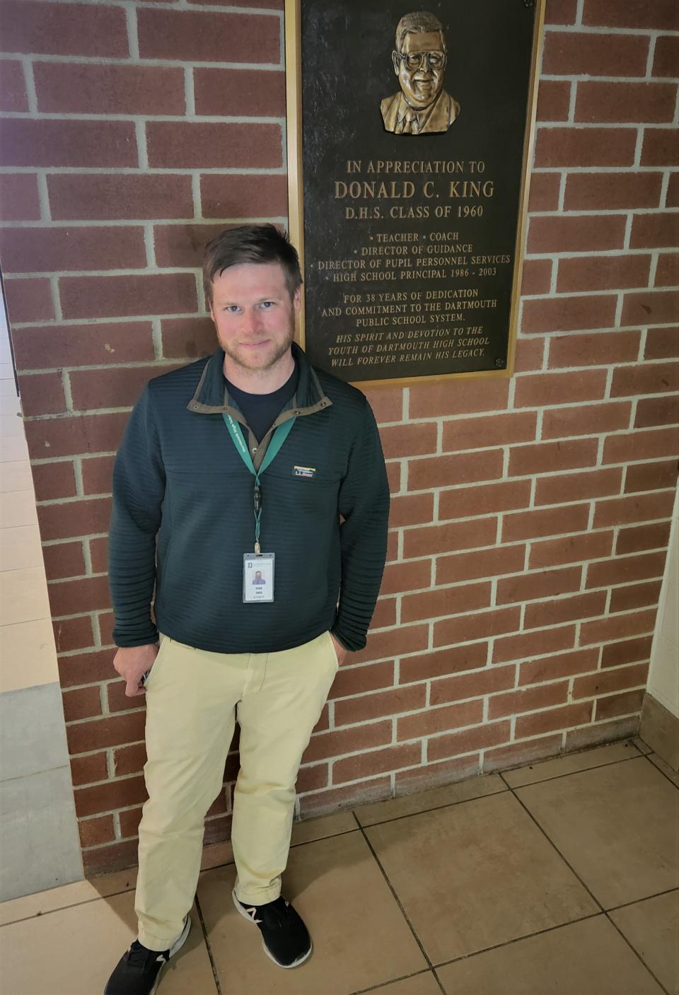 Ryan Shea, a Dartmouth native, is a 2001 graduate of Dartmouth High School and now its principal. Here he is seen with a plaque in Dartmouth High's main lobby dedicated to Donald King, who was principal when Shea was a student.