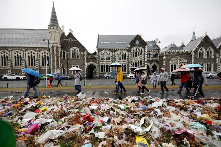 People walk past flowers and tributes displayed in memory of the twin mosque massacre victims outside the Botanical Gardens in Christchurch on April 5, 2019. - The man accused of shooting dead 50 Muslim worshippers in a Christchurch mosque sat impassively April 5 as a New Zealand judge ordered him to undergo tests to determine if he is mentally fit to stand trial for murder. (Photo by Sanka VIDANAGAMA / AFP)        (Photo credit should read SANKA VIDANAGAMA/AFP/Getty Images)