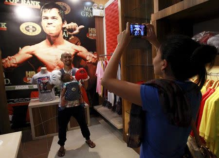 A woman uses a mobile phone to take pictures of her husband posing in front of a poster of boxer Manny Pacquiao of the Philippines on display at a mall in Manila April 24, 2015. Pacquiao is scheduled to fight Floyd Mayweather of the U.S. on May 2, 2015 in Las Vegas, Nevada. REUTERS/Romeo Ranoco