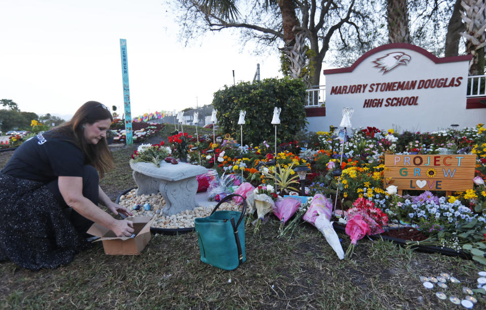 FILE - Suzanne Devine Clark, an art teacher at Deerfield Beach Elementary School, places painted stones at a memorial outside Marjory Stoneman Douglas High School during the first anniversary of the school shooting in Parkland, Fla., Feb. 14, 2019. The 2018 Parkland high school massacre will be reenacted with the firing of about 140 blanks on campus as part of families' lawsuits against the former sheriff's deputy they accuse of failing to stop the gunman, a judge ruled Wednesday, July 12, 2023. (AP Photo/Wilfredo Lee, File)
