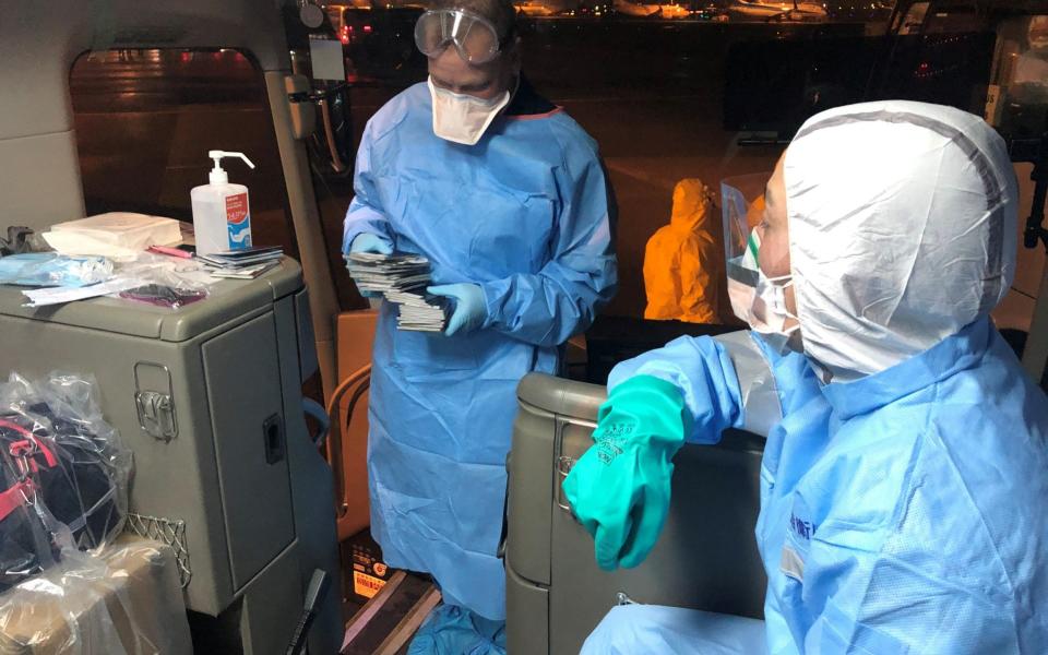 Health officials in protective suits prepare a shuttle bus transporting U.S. passengers who have chosen to leave the Diamond Princess cruise ship, to a chartered evacuation aircraft at Haneda airport in Japan -  Philip and Gay Courter / Reuters