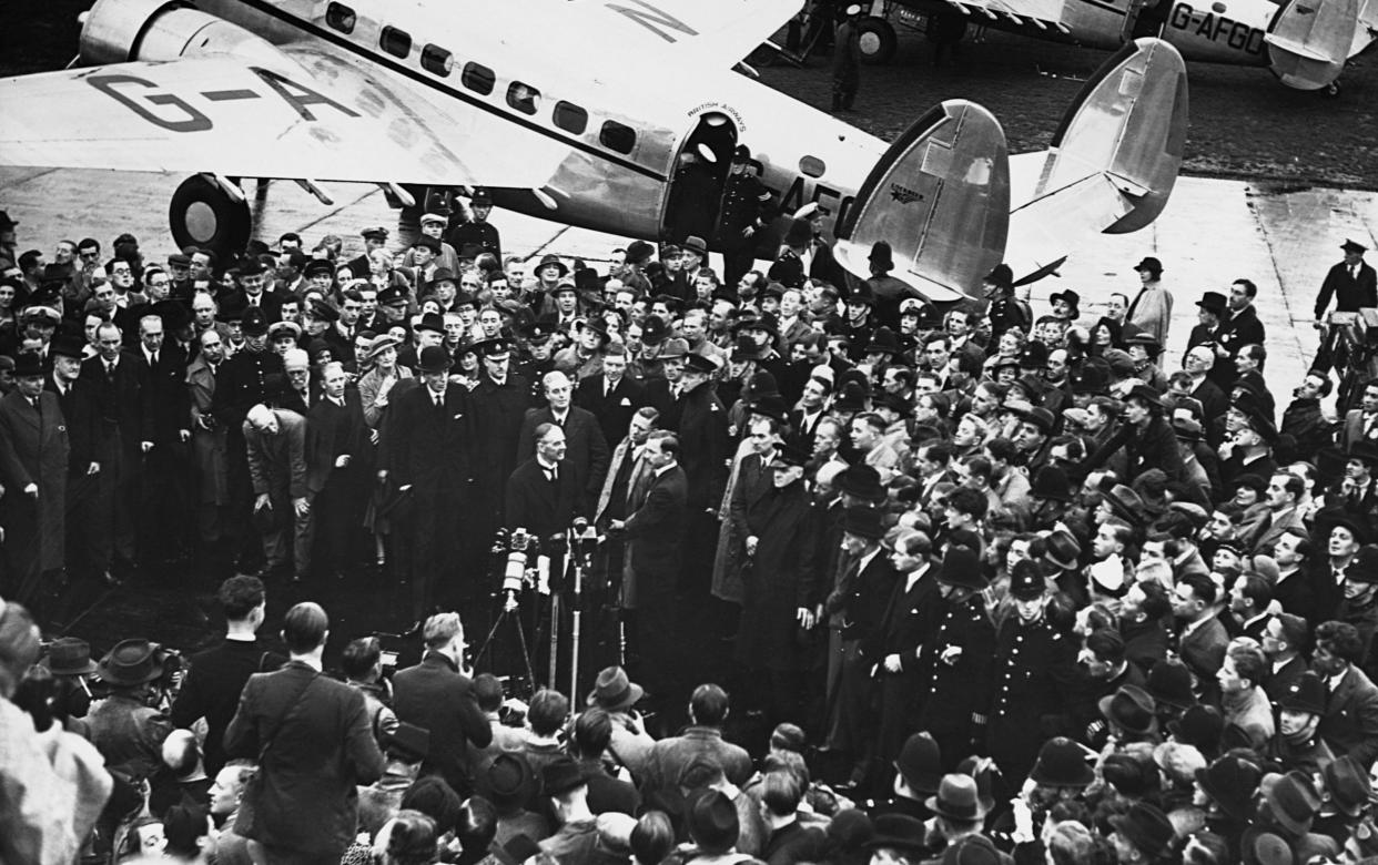 A throng of people press around the prime minister in a black and white image from a high angle, with the plane he flew on clearly visible behind