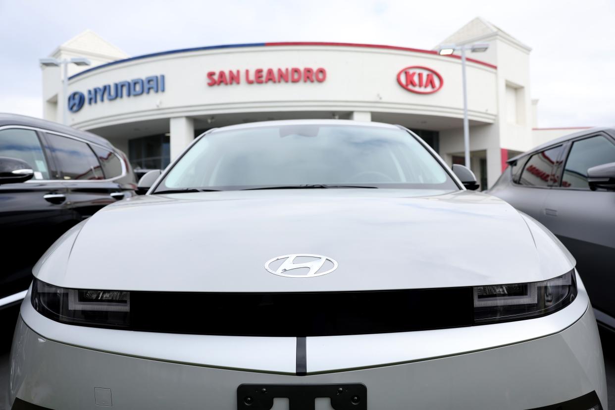 A close-up of a Hyundai, with the Hyundai and Kia logos on a building behind it