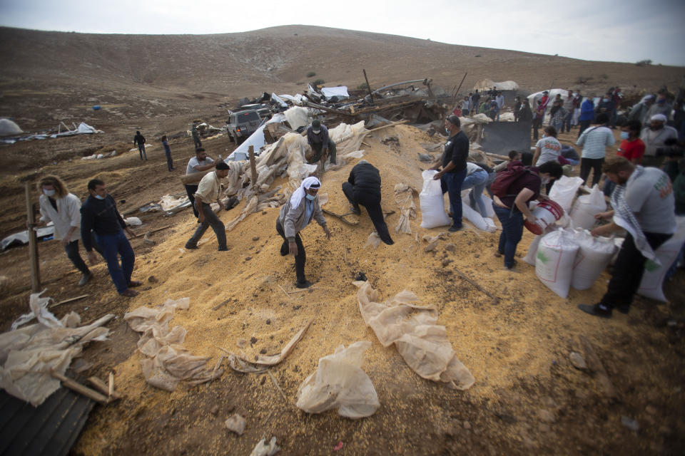 Palestinians collect grain aftre Israeli military destroyed storage structure n Khirbet Humsu in Jordan Valley in the West Bank, Friday, Nov. 6, 2020. Israeli troops with bulldozers and heavy equipment demolished 18 tents and other structures that housed 74 people, including 41 minors, according to the Israeli rights group B'Tselem. COGAT, the Israeli military body in charge of civilian affairs in the West Bank, said an "enforcement activity" was carried out against seven tents and eight pens that were "illegally constructed" in a firing range. (AP Photo/Majdi Mohammed)