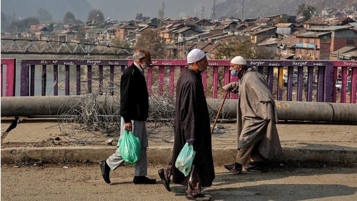Elderly men walk over a bridge on a cold winter day as residential houses are seen in the background in Baramulla Jammu and Kashmir India on 25 November 2022