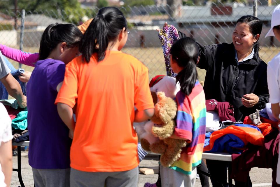 A woman smiles as she offers clothing to others during a clothing giveaway event outdoors