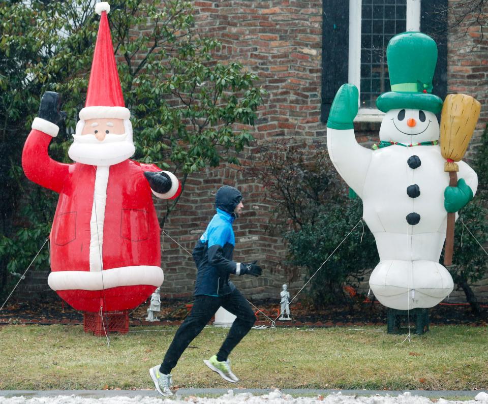 A man runs in the rain past an inflatable Santa and snowman on Washington Avenue in Albany, N.Y.