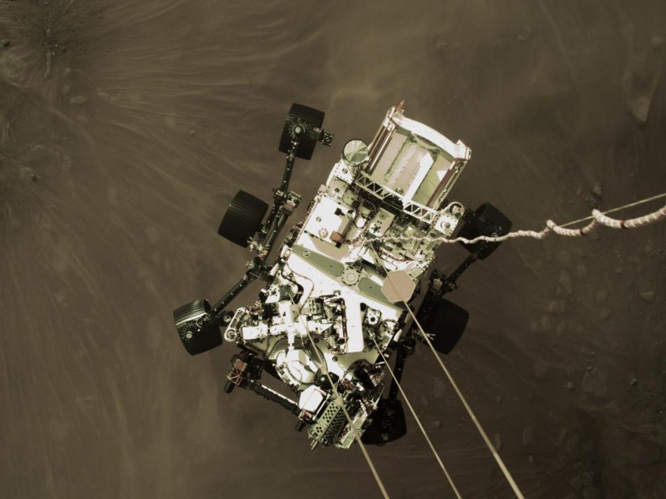 An above shot of a rover landing on a brown surface.