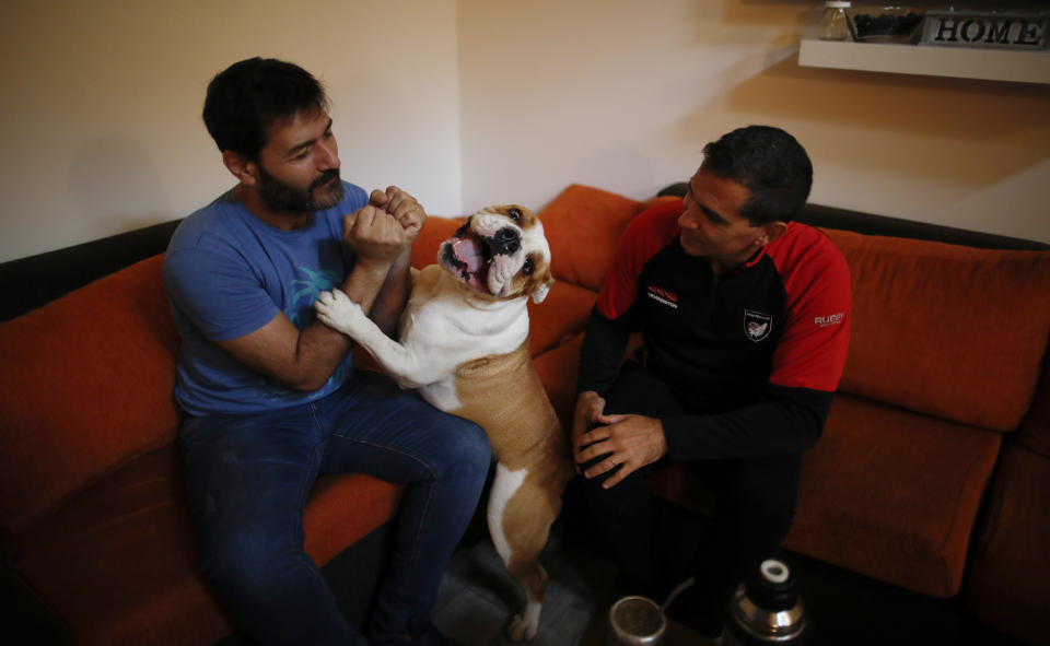 El exsacerdote católico Andrés Gioeni, a la derecha, se sienta con su esposo Luis Iarocci y su perro Boris después de que regresaron a casa del obispado donde comenzó el proceso de apostasía en Buenos Aires, Argentina, el miércoles 17 de marzo de 2021. (AP Foto/Natacha Pisarenko)