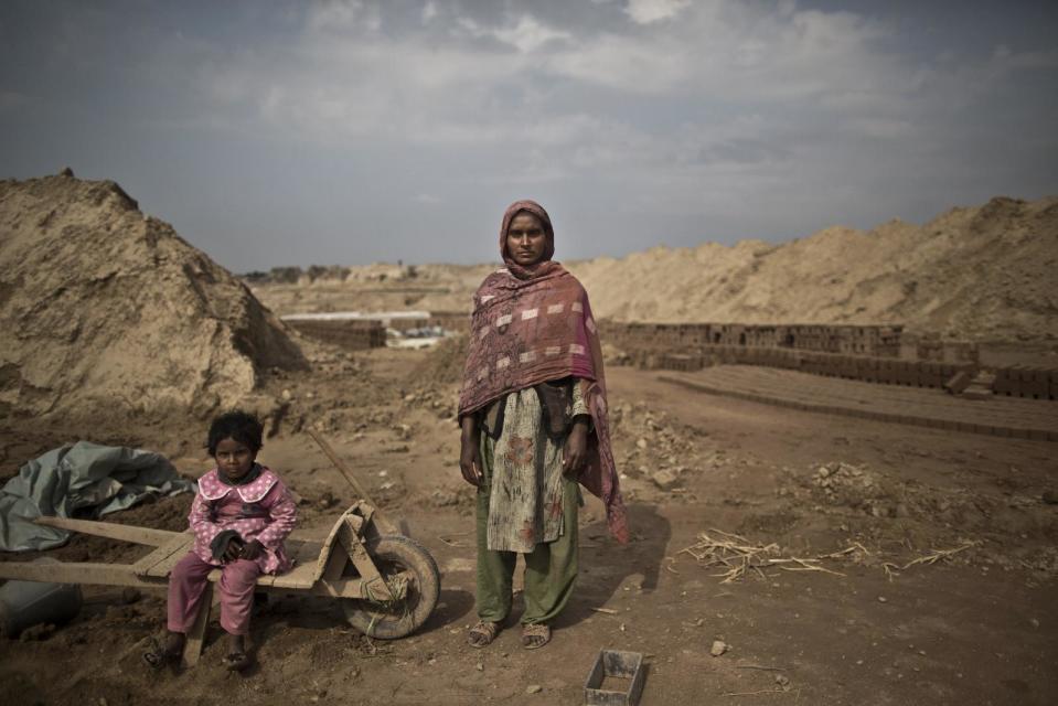 In this Wednesday, March 5, 2014, photo, Sofia Zahour, 25, a Pakistani brick factory worker, poses for a picture as standing next to her daughter Alina, 2, at the site of her work in Mandra, near Rawalpindi, Pakistan. Sofia and her husband are in debt for their employer the amount of 400,000 rupees (approximately $4000). (AP Photo/Muhammed Muheisen)