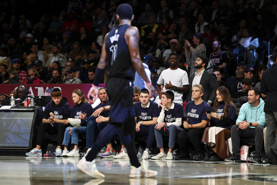 Fans with matching shirts look on as Brooklyn Nets guard Kyrie Irving (11) walks by during the first half of an NBA basketball game against the Indiana Pacers, Monday, Oct. 31, 2022, in New York. (AP Photo/Jessie Alcheh)