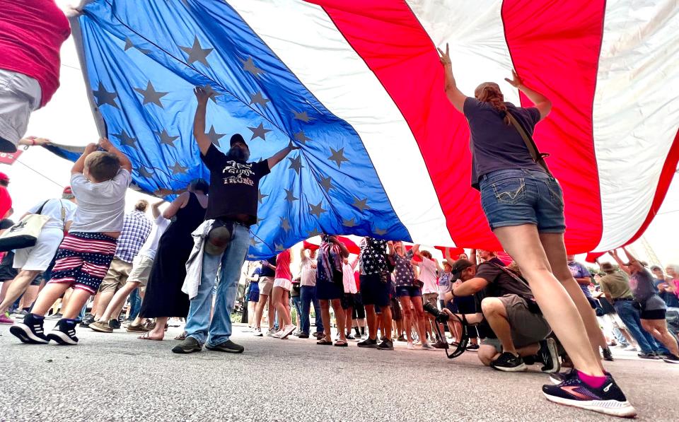 Steve Hollingsworth of Greenwood helps hold up a large US flag while waiting in line before the Donald Trump visit on Saturday, July 1, 2023, in Pickens, SC.