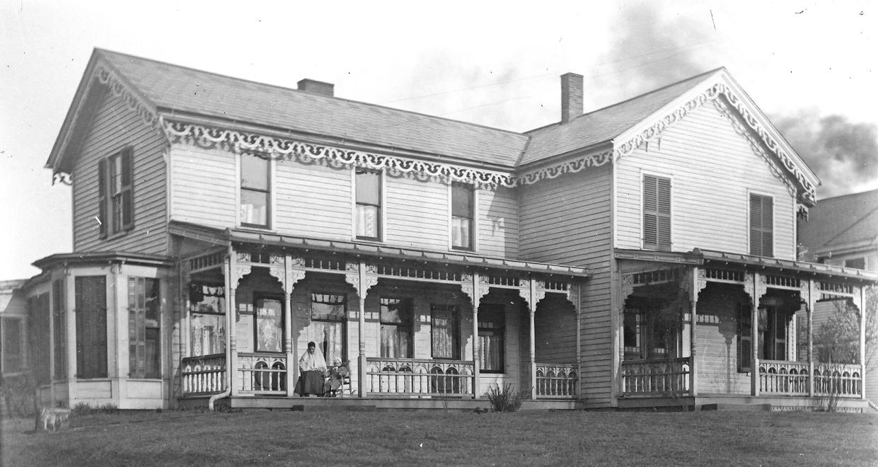 Such a beautiful home! Do you see the woman and toddler sitting in rocking chairs on the porch? This picture was taken at the turn of the 20th century. Where is it?