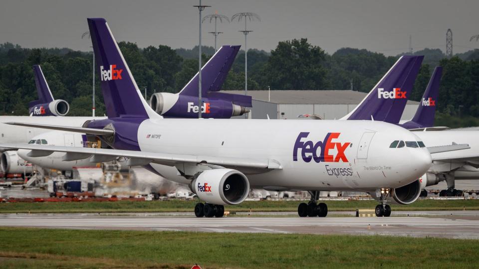 Purple-tailed FedEx planes parked in the background as another jet rolls down the taxiway.