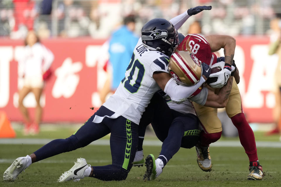 San Francisco 49ers tight end George Kittle (85) is tackled by Seattle Seahawks safety Julian Love (20) and linebacker Bobby Wagner during the first half of an NFL football game in Santa Clara, Calif., Sunday, Dec. 10, 2023. (AP Photo/Godofredo A. Vásquez)