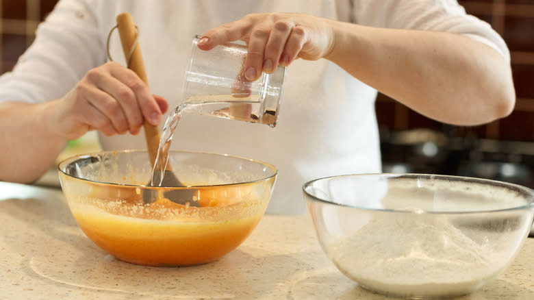 Hands pouring water into a bowl of cake mix