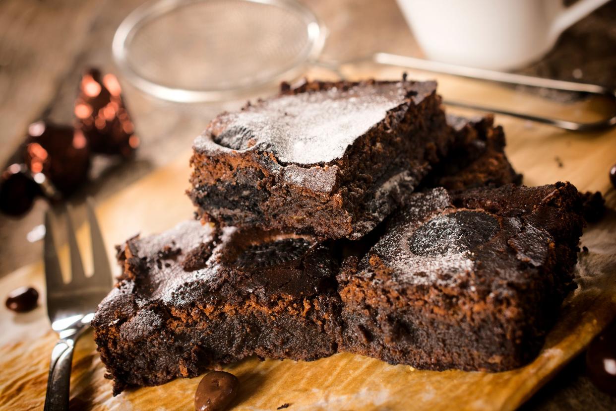 Gooey double-chocolate brownies on a wooden cutting board with a fork with a blurred background of baking utensils