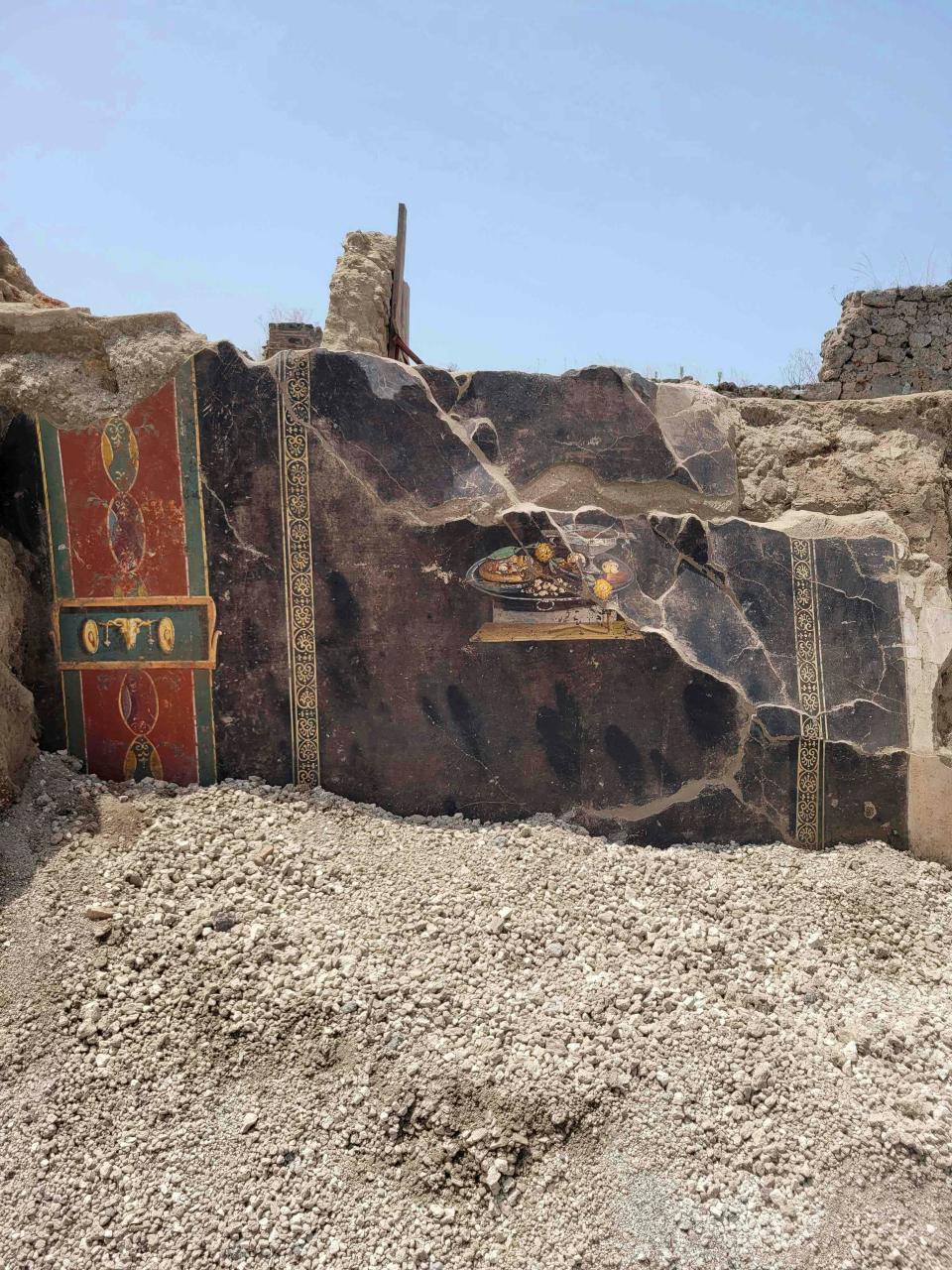This picture provided on Tuesday, June 27, 2023, by the Pompeii Archaeological Park shows the wall of an ancient Pompeian house with frescoes, one depicting a table with food. The fresco was found in the atrium of a house in Insula 10 of Regio IX under excavation, to which a bakery was annexed, already partially explored between 1888 and 1891 and whose investigations were resumed last January. (Pompeii Archaeological Park via AP, ho)