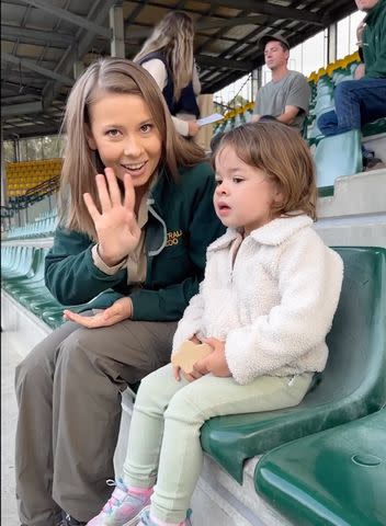 <p>bindisueirwin/Instagram</p> Bindi Irwin waves at the camera as she sits with 2-year-old daughter Grace at the zoo's crocoseum.