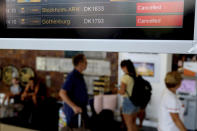 Passengers pass by a flights screen showing two cancelled flights of Thomas Cook at Larnaca airport in the eastern Mediterranean island of Cyprus, Monday, Sept. 23, 2019. The collapse of Thomas Cook will strike a major blow to the Cypriot tourism industry. (AP Photo/Petros Karadjias)