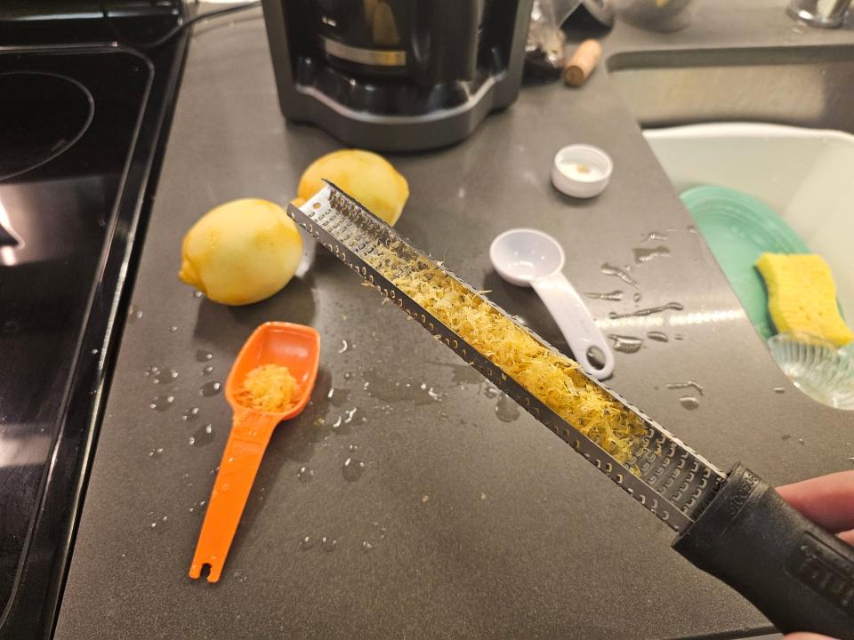 Microplane zester filled with lemon zest above two shaved lemons