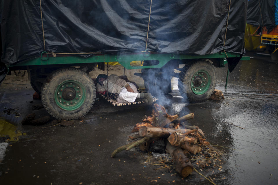 FILE - In this Monday, Jan. 4, 2021, file photo, a farmer lies under the belly of a tractor trolley next to a bonfire as they block a major highway in protest against new farm laws while it rains at the Delhi-Uttar Pradesh state border, India. The protests gained momentum in November when the farmers tried to march into New Delhi but were stopped by police. Since then, they have promised to hunker down at the edge of the city until the laws are repealed. (AP Photo/Altaf Qadri, File)
