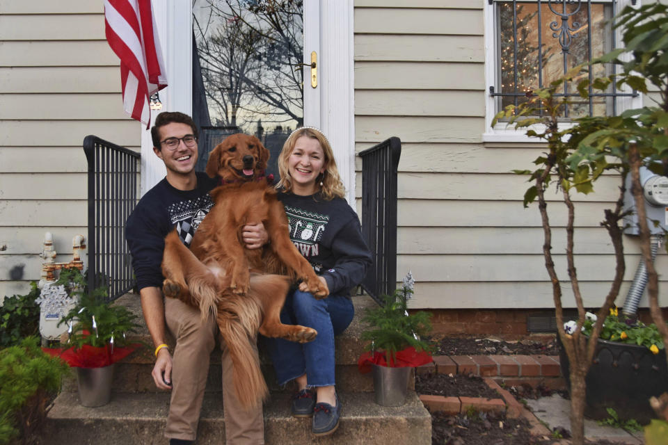 In this photo provided by Olivia Hinerfeld, Olivia Hinerfeld poses with her boyfriend, Ryan Shymansky, and their golden retriever Lincoln on Dec. 6, 2020, in Washington. Jealous of the attention that Hinerfeld is paying to her video conference call, Lincoln,will fetch “the most disgusting” tennis ball he can find from his toy crate to drop into the lap of the Georgetown University Law School student. (Olivia Hinerfeld via AP)