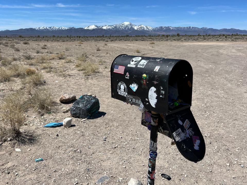 A black mailbox covered in stickers in the middle of the desert.