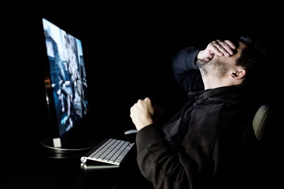 A man at a computer holding his head in his hand.