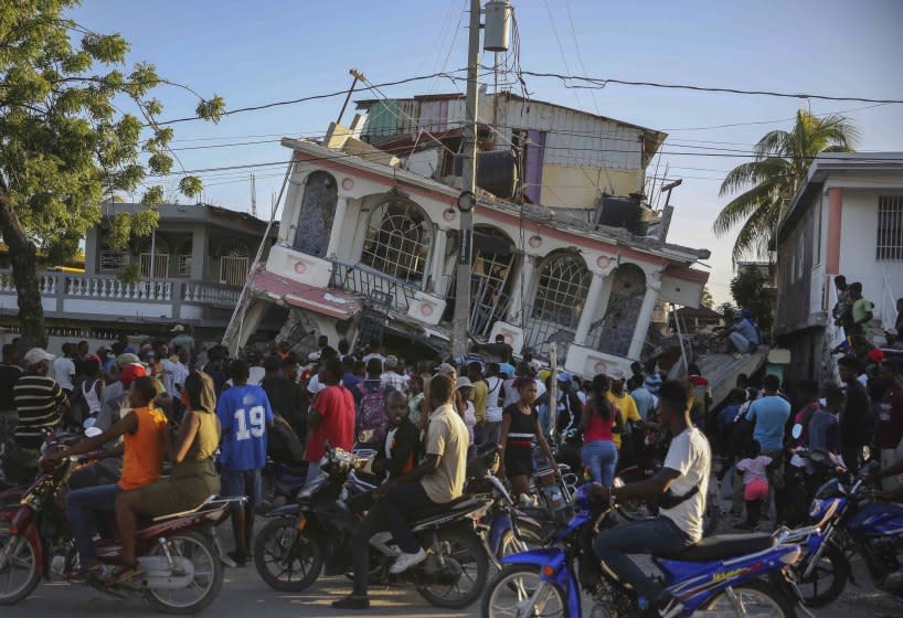 People gather outside the Petit Pas Hotel, destroyed by the earthquake in Les Cayes, Haiti, Saturday, Aug. 14, 2021. A 7.2 magnitude earthquake struck Haiti on Saturday, with the epicenter about 125 kilometers (78 miles) west of the capital of Port-au-Prince, the US Geological Survey said. (AP Photo/Joseph Odelyn)